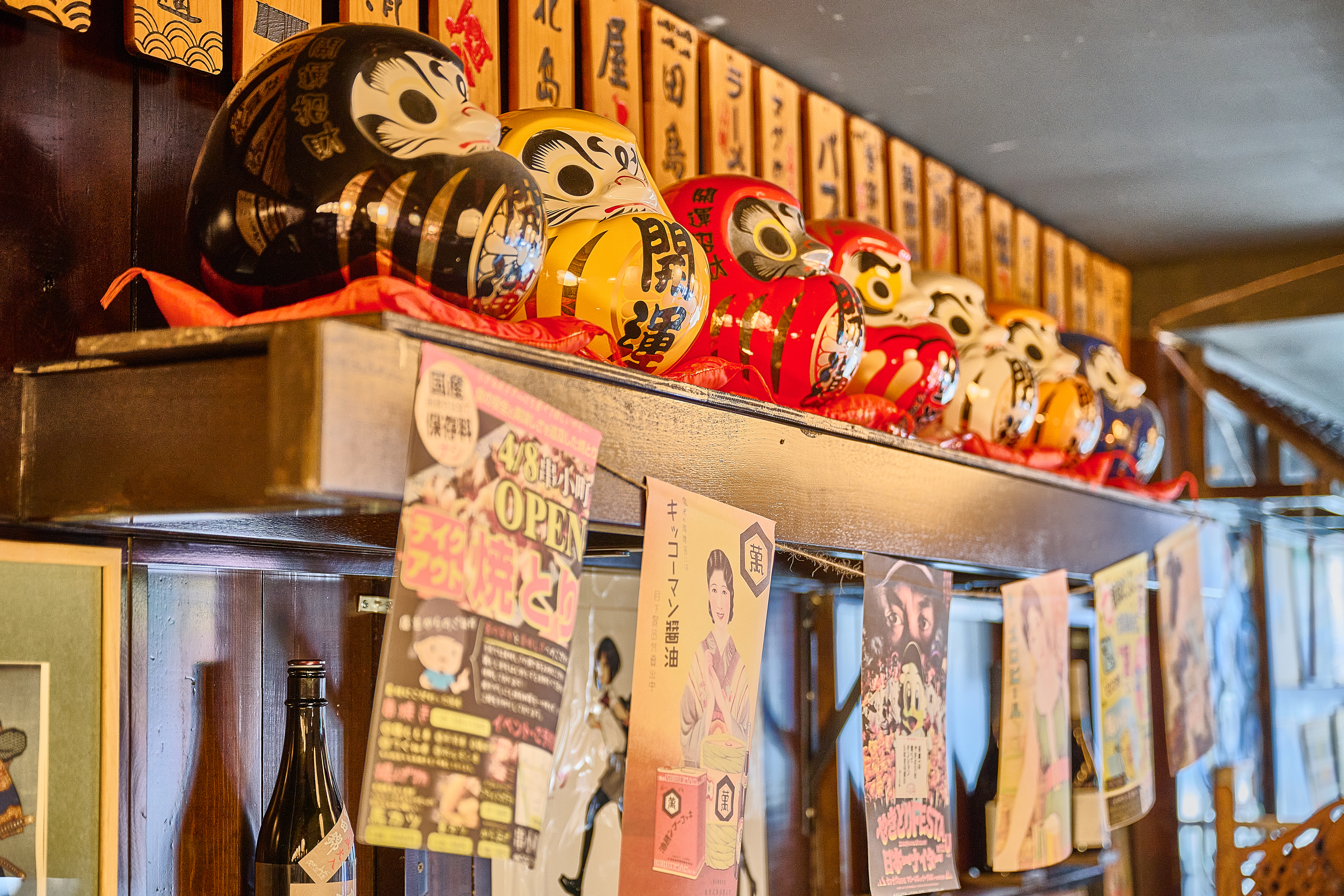 Collection of traditional daruma dolls and sake bottles displayed on shelf at Showa Era Izakaya