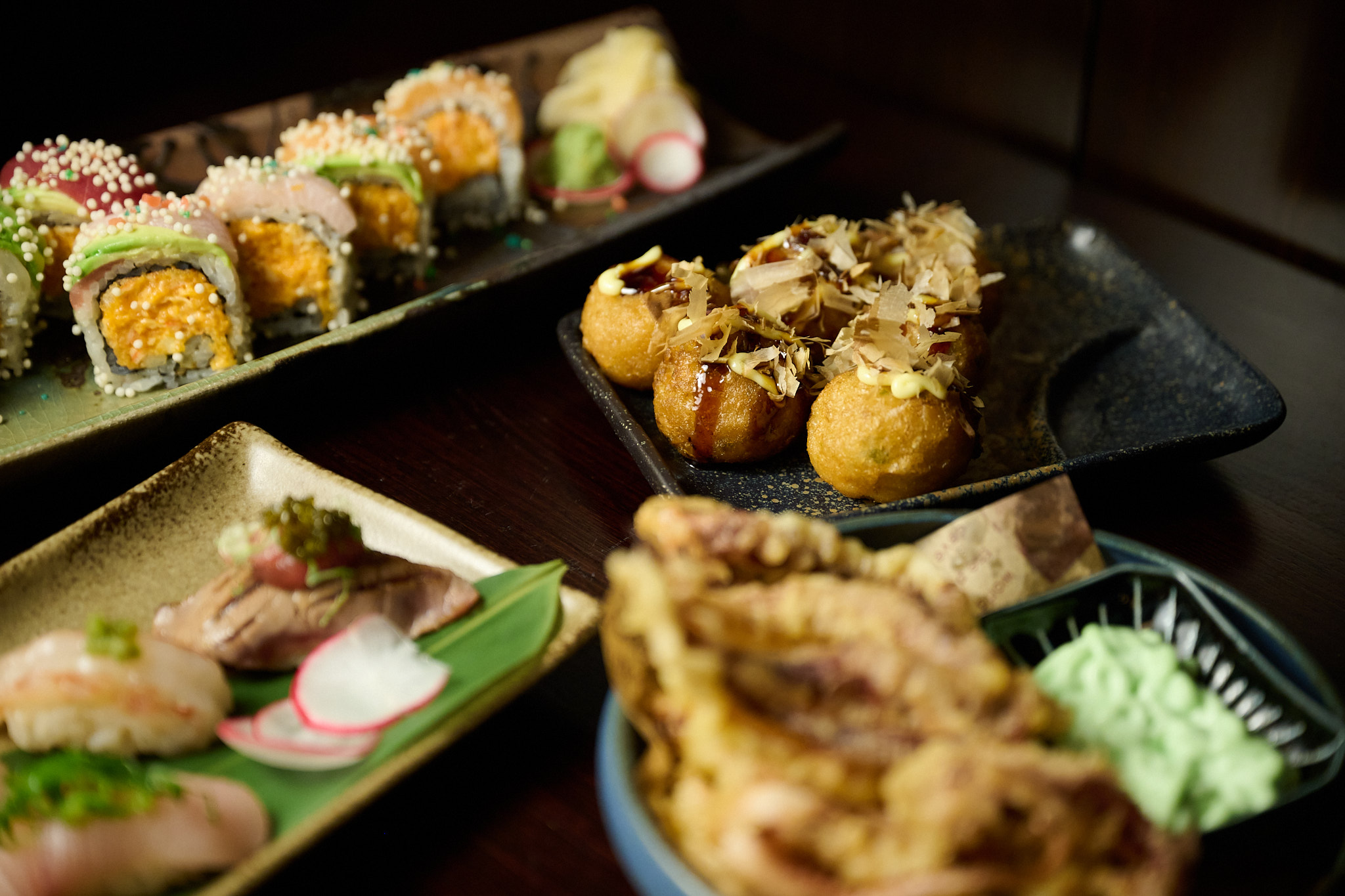 Multiple Japanese dishes spread on izakaya table including sushi, takoyaki, tempura, and rolls at Showa Era