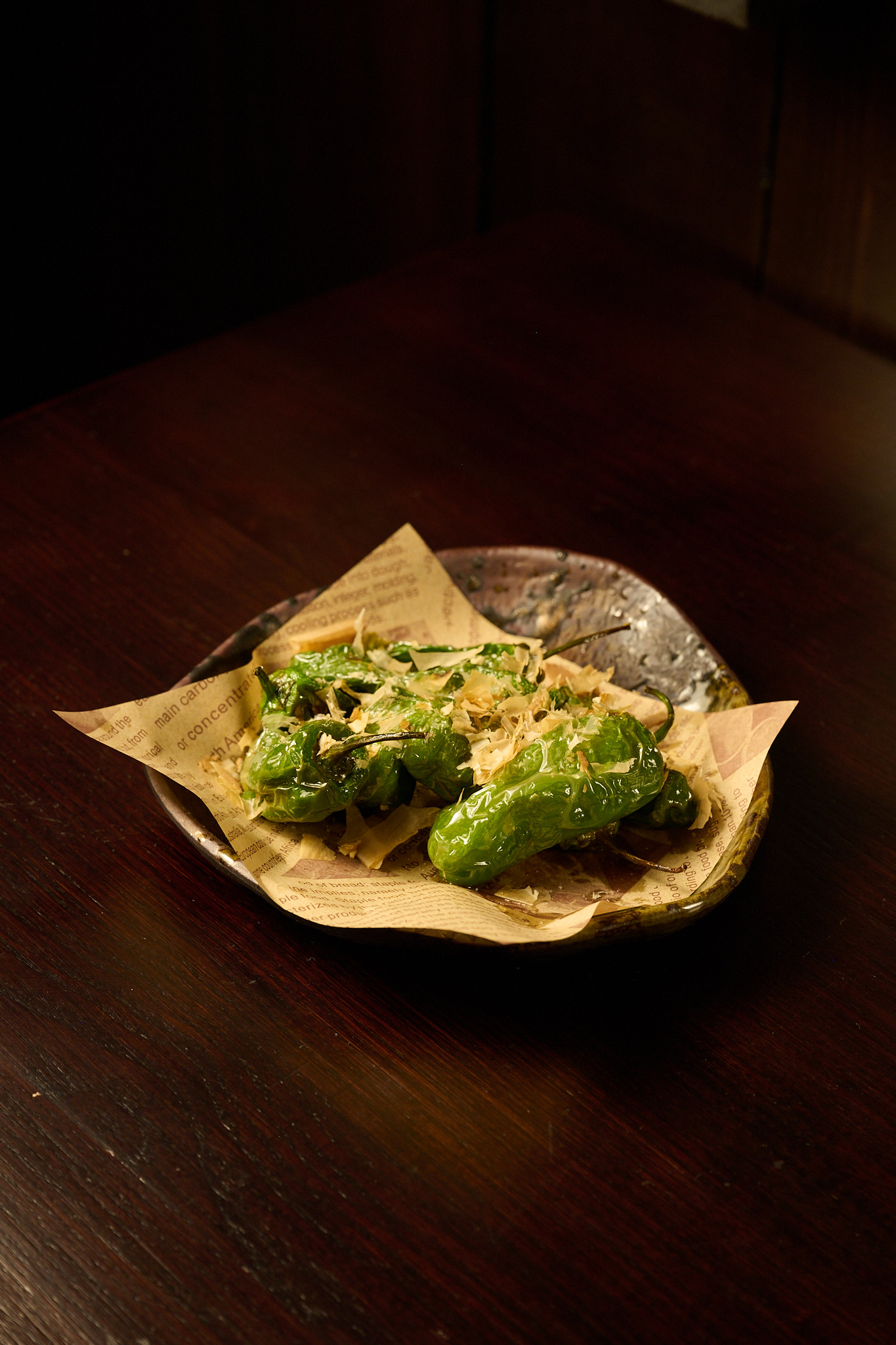 Blistered shishito peppers topped with bonito flakes served on newspaper-lined ceramic plate at Showa Era