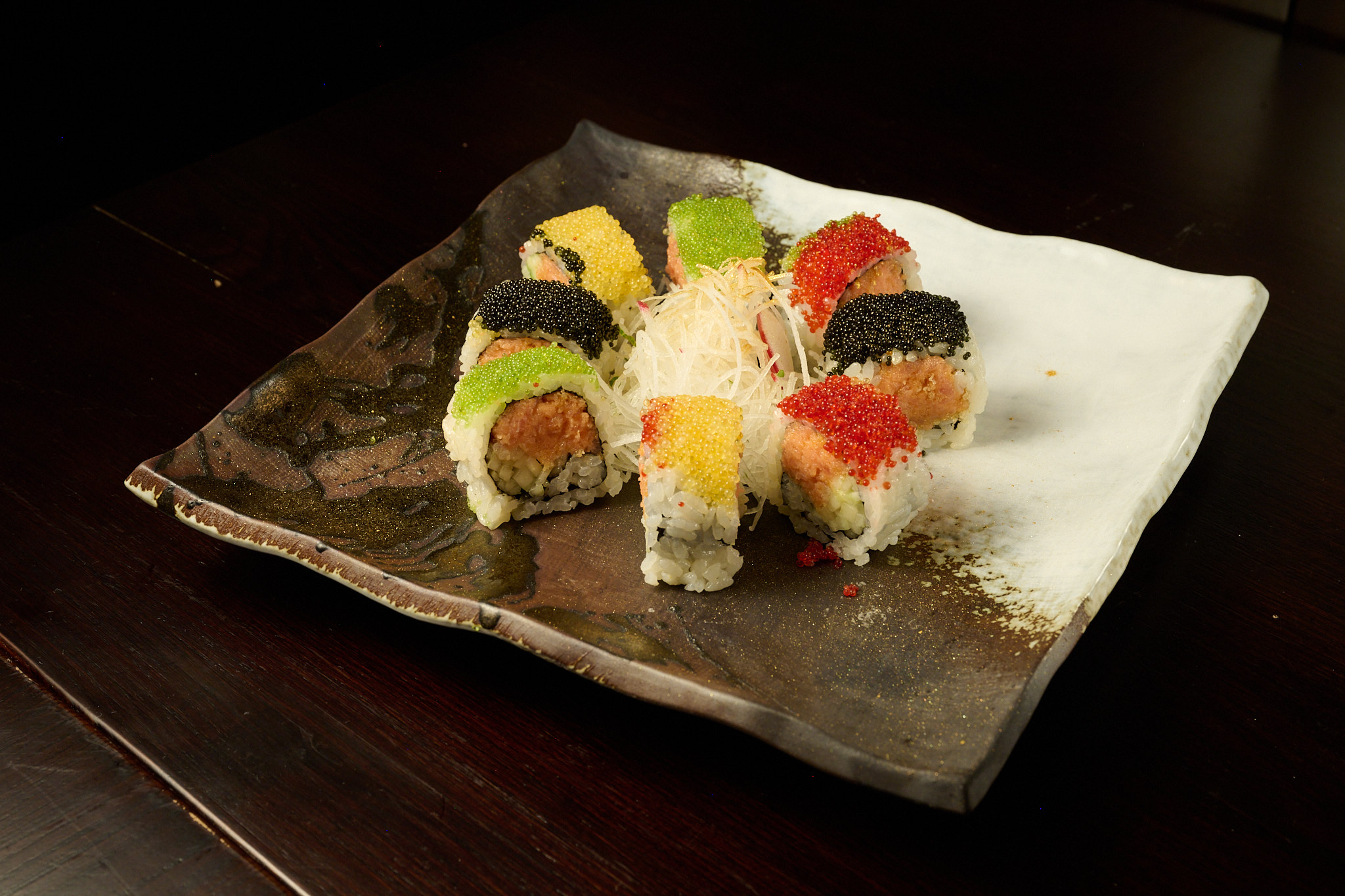 Artisan sushi roll topped with multicolored tobiko caviar on handcrafted ceramic plate at Showa Era