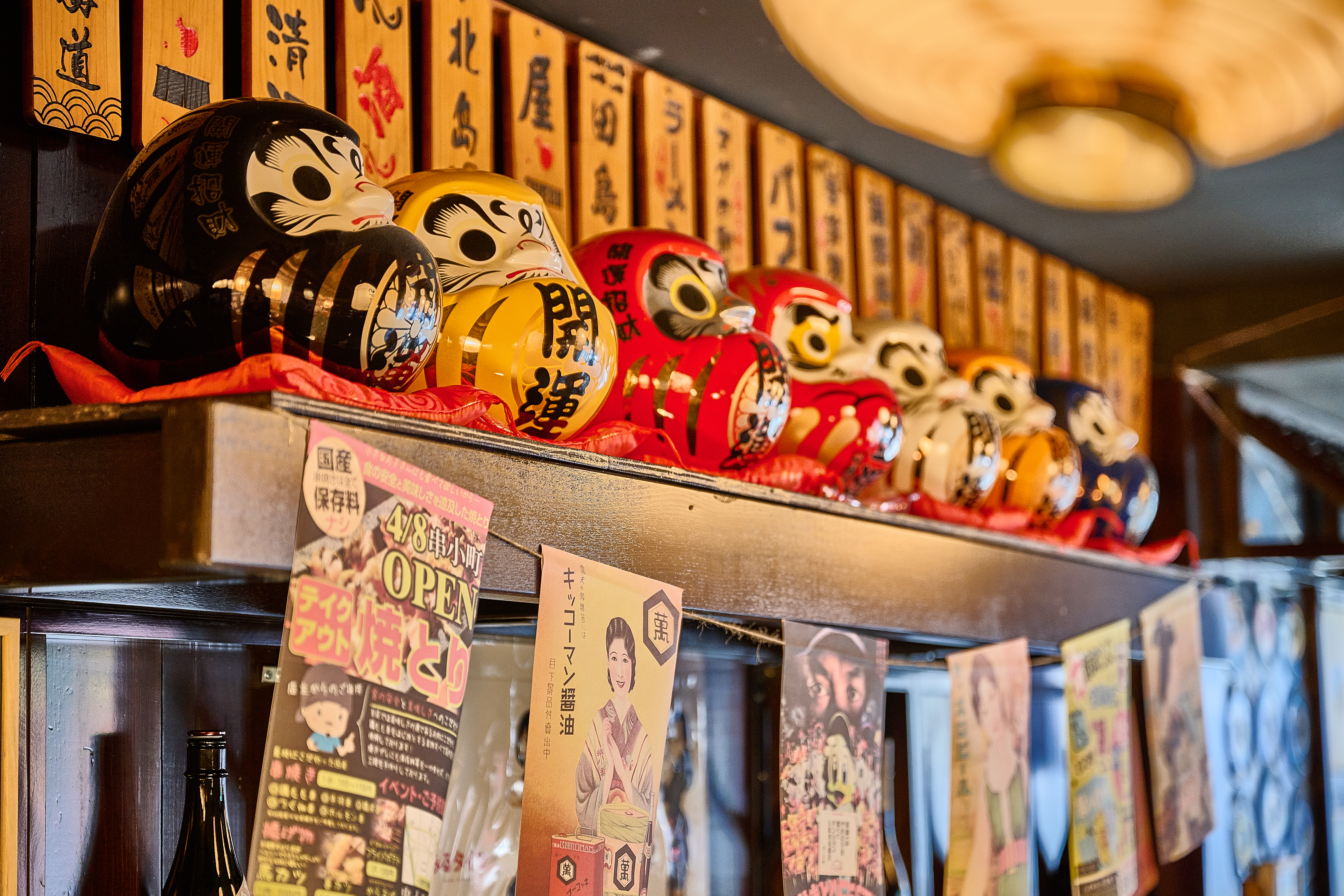 Colorful daruma doll collection on shelf with vintage Japanese posters at Showa Era NYC