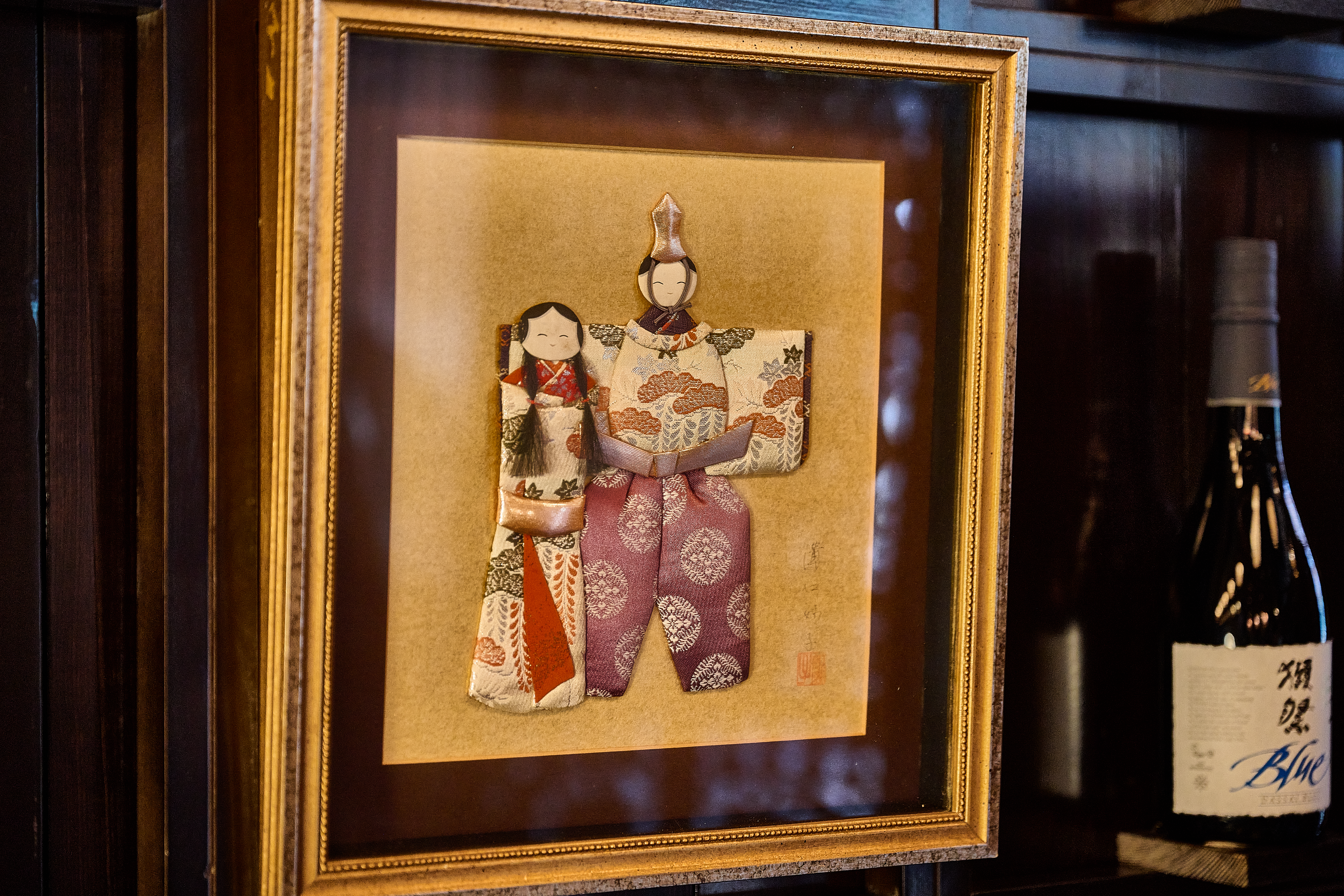 Framed Japanese traditional doll artwork next to premium Dassai sake at Showa Era