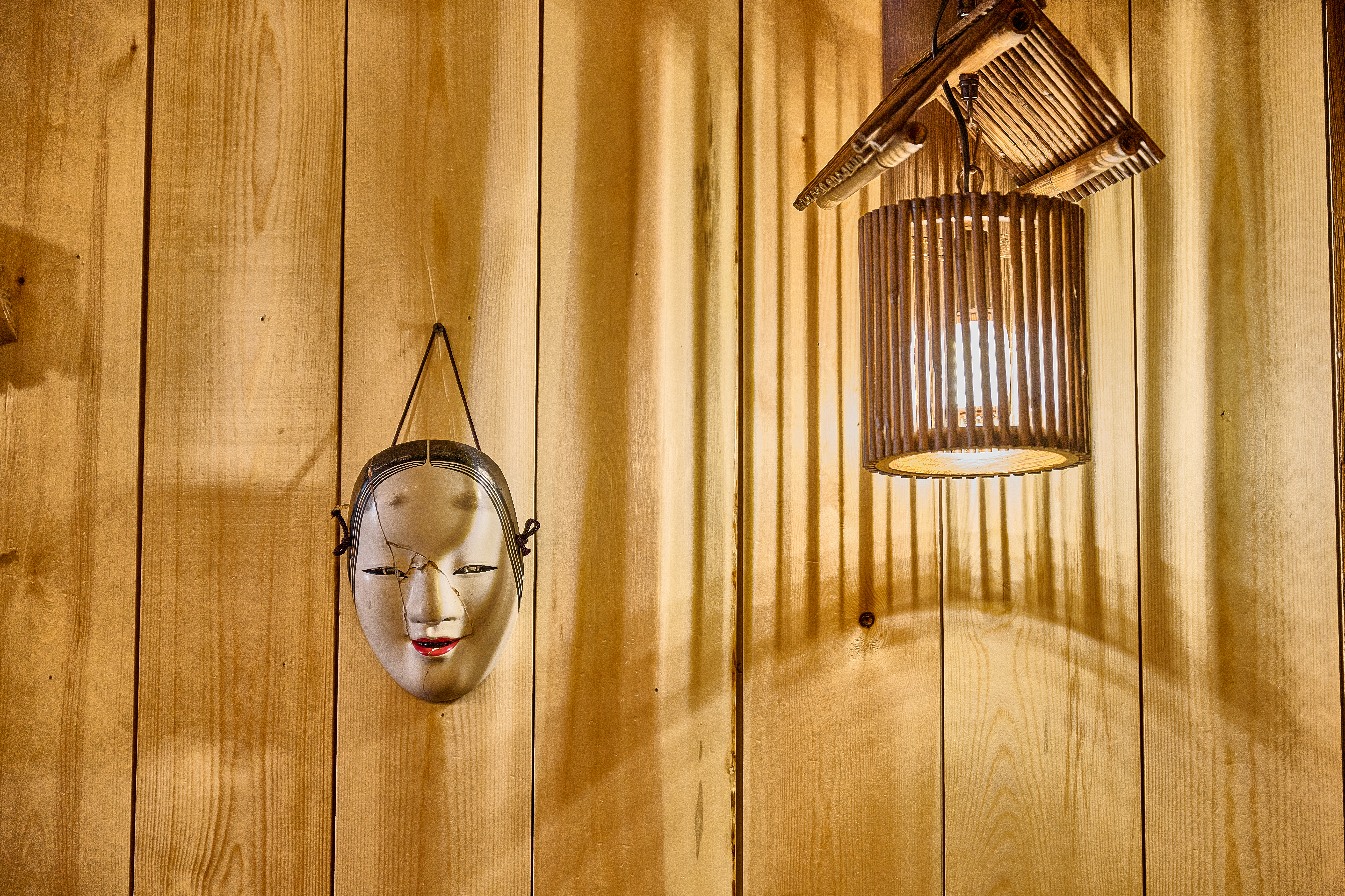 Traditional Noh mask and bamboo lantern on warm wood wall at Showa Era Izakaya
